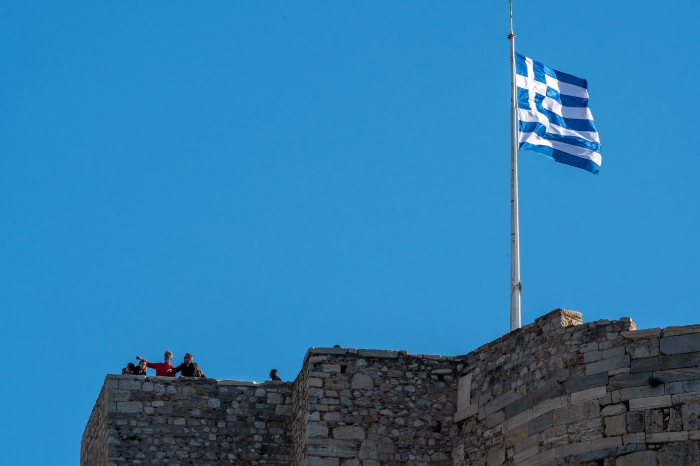 The Greek flag on the medieval lookout tower with tourists enjoying the fantastic view over Athens