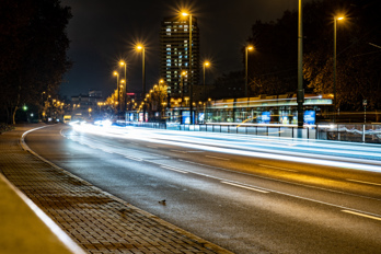 Long exposure image at night. Light trails from moving cars and light poles with starbursts. Skyscraper and a Street Tram in background  Carl-Bosch-Straße, Ludwigshafen am Rhein