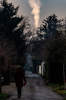 Gravel road with smoking chimney in the background