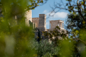 The monument to Agrippa and the temple of Athena Nike seen from the northern side of the Agora, surrounded by the leaves of the trees.