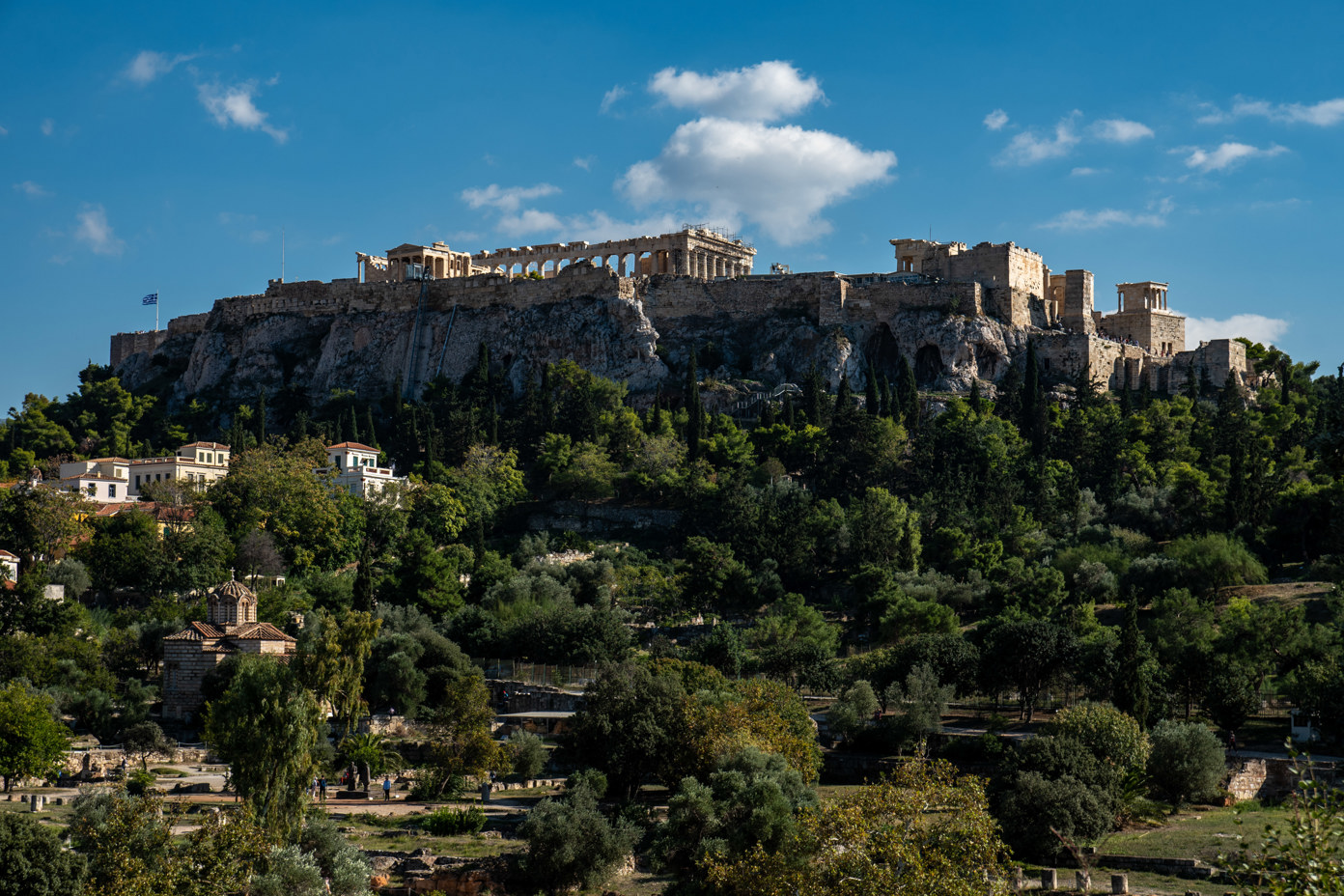 The acropolis from the Hephaistos temple. On the left, the viewing platform with the flagpole and the Hellenic flag. In the middle, the Temple of Erechtheion in front and the Parthenon behind. On the right the Propylaea with the Monument of Agrippa and on the far right the Temple of Athena Nike.