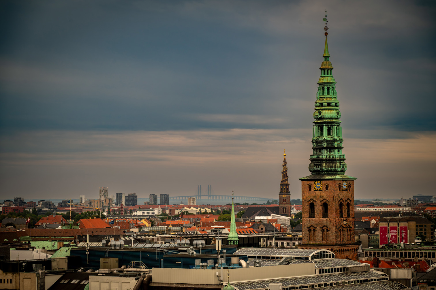 View from the Round Tower (Rundetaarn), an astronomical tower almost 40 meters high in Copenhagen's city center. In the foreground on the right is the tower of the Nikolaj Art Center. To the left is the spiral tower of Vor Frelsers Kirke (Stairway to Heaven). In the background the Øresund Bridge connecting Denmark with Sweden.