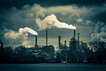 Industrial plants with smoking chimneys. In the foreground a field.