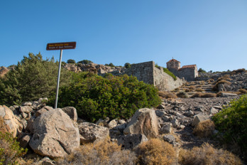 The remains of the Temple of Zeus Hellanios on the island of Aegina are hidden under bushes. In the background is the small Byzantine church of Taxiarches on Aigina.