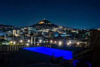 Long exposure shot of Athens at night. In the foreground a roof terrace in blue and street lamps with aperture stars. Mount Lycabettus in the background.